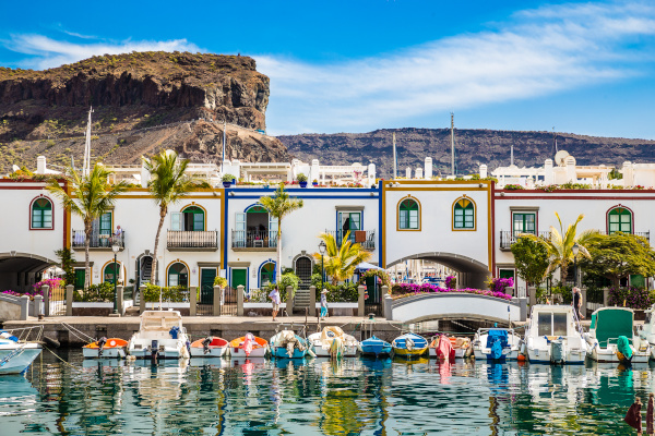 Traditional Colorful Buildings With Boats In Front And Mountain In The Backsground - Puerto de Mogan, Gran Canaria, Canary Islands, Spain