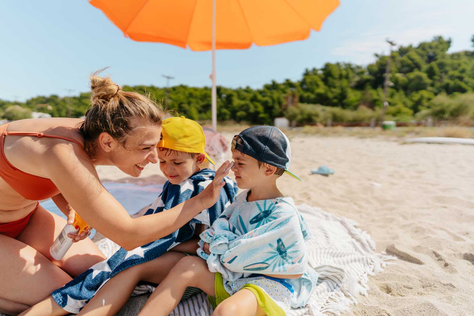 Mutter trägt am Strand ihren Jungs Sonnencreme auf.