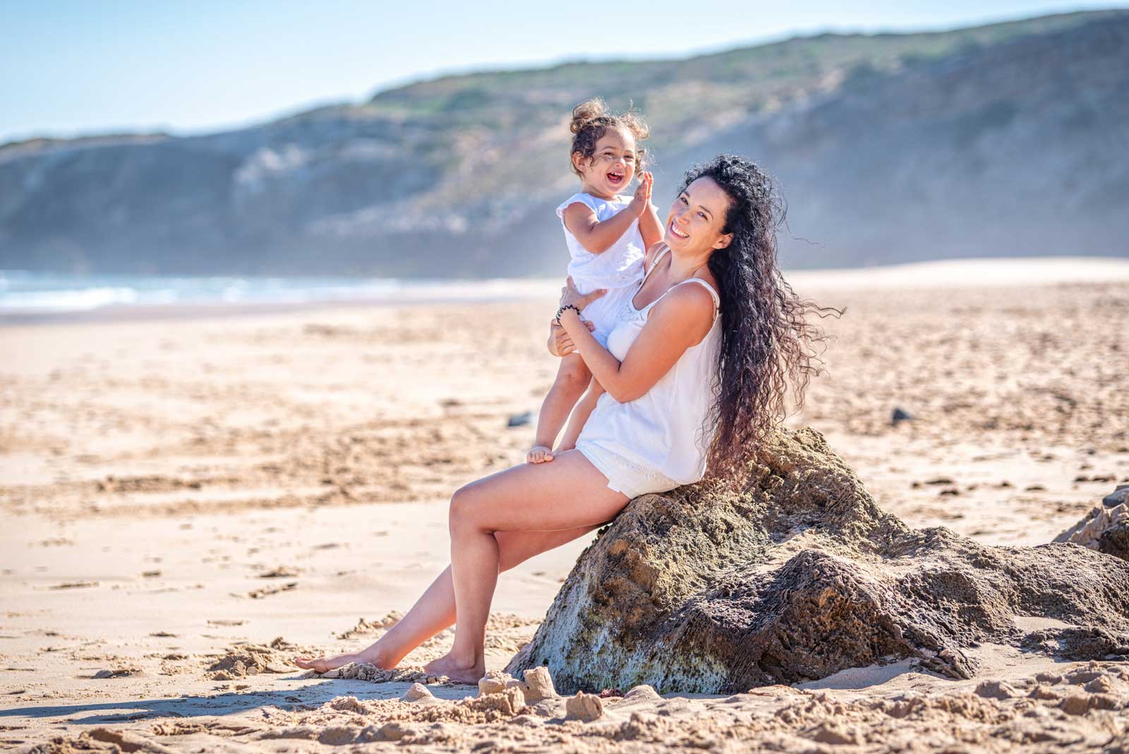Mutter und Tochter sitzen auf einem Felsen am Strand der Algarve in Portugal.